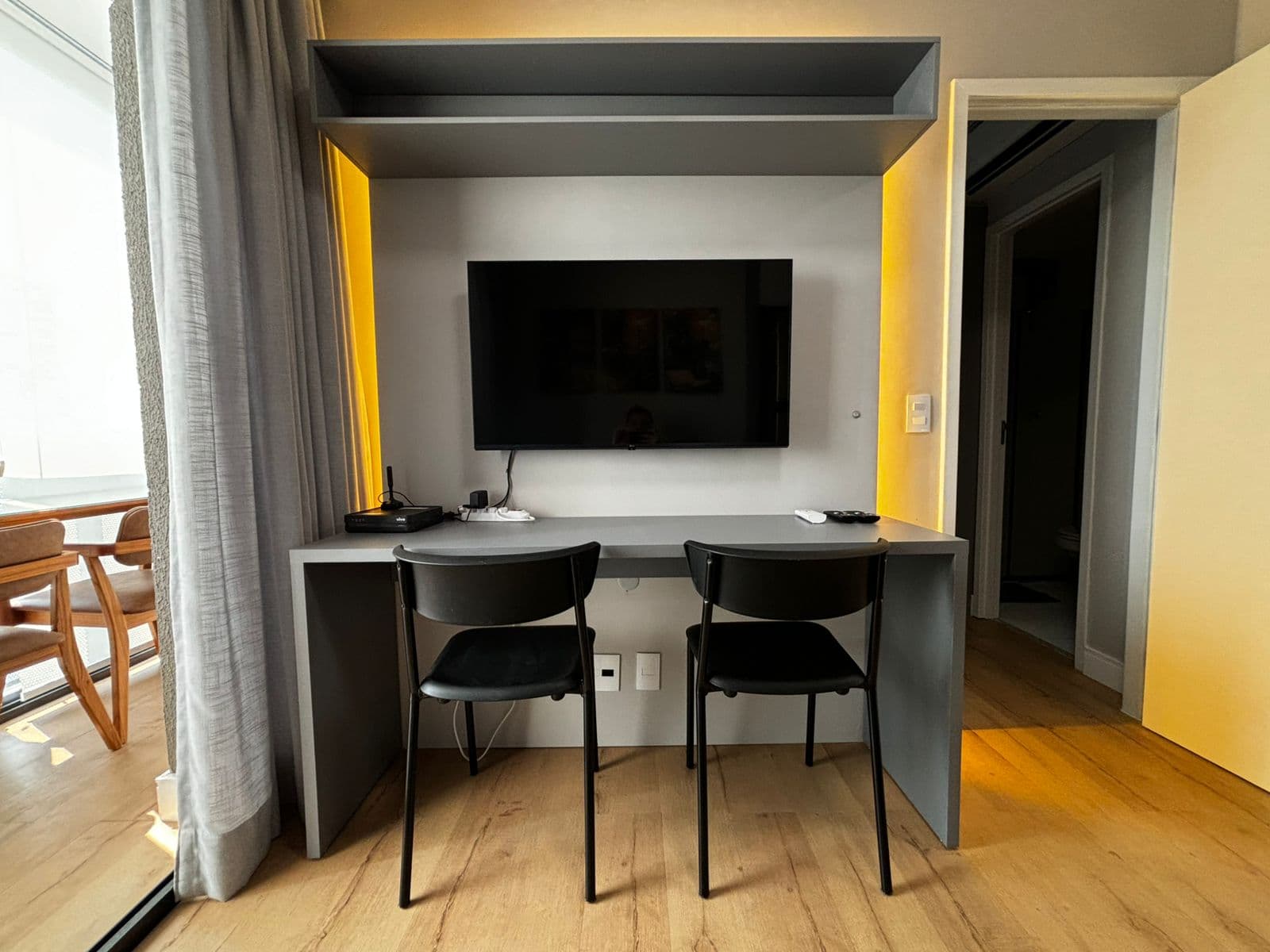 Painel de TV com bancada de estudos, duas cadeiras pretas e iluminação em LED embutida.