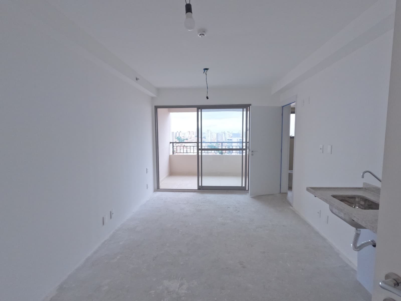 Ambiente interno integrado com piso em acabamento bruto, pia de cozinha e porta de vidro para a varanda.